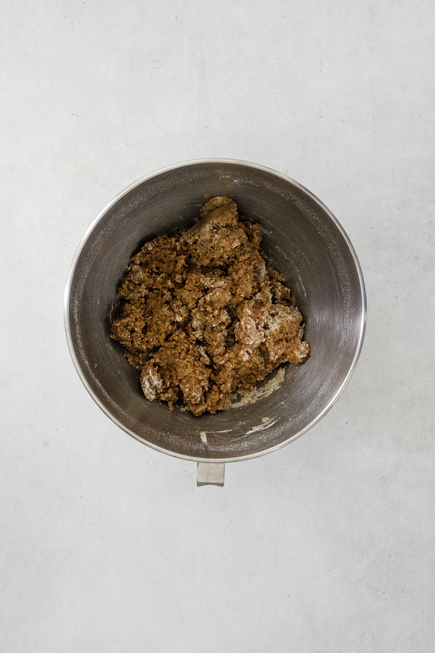 A metal mixing bowl containing a chunky brown Pumpkin Banana bundt cake dough mixture sits on a light gray surface.