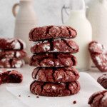 a stack of red velvet cake cookies amongst glasses of milk