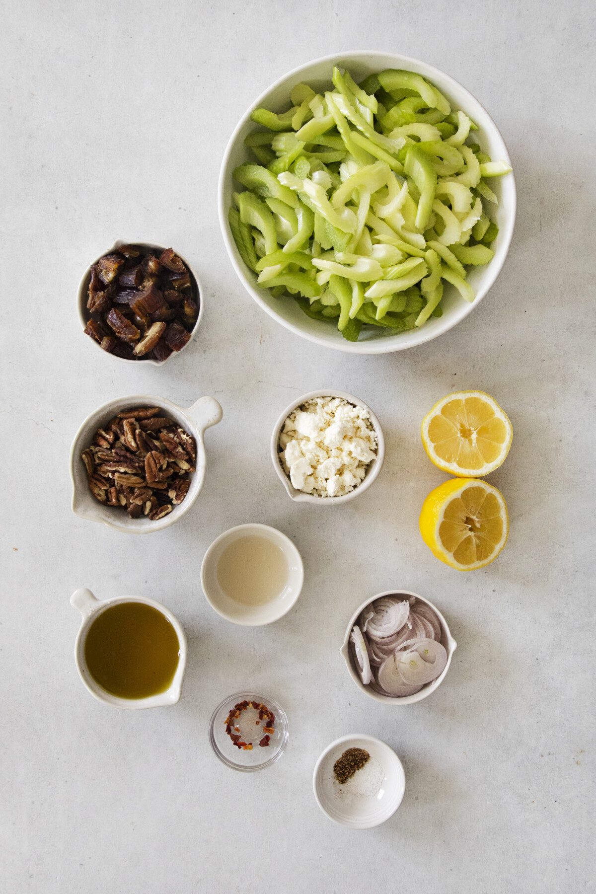 small ceramic bowls of ingredients: celery, lemon halves, oil, shallots, dates, nuts