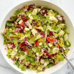 A large white bowl filled with a vibrant Vegetarian Chopped Antipasto Salad, featuring lettuce, radicchio, artichoke hearts, tomatoes, pepperoncini, and cheese, all tossed together with a serving spoon inside.