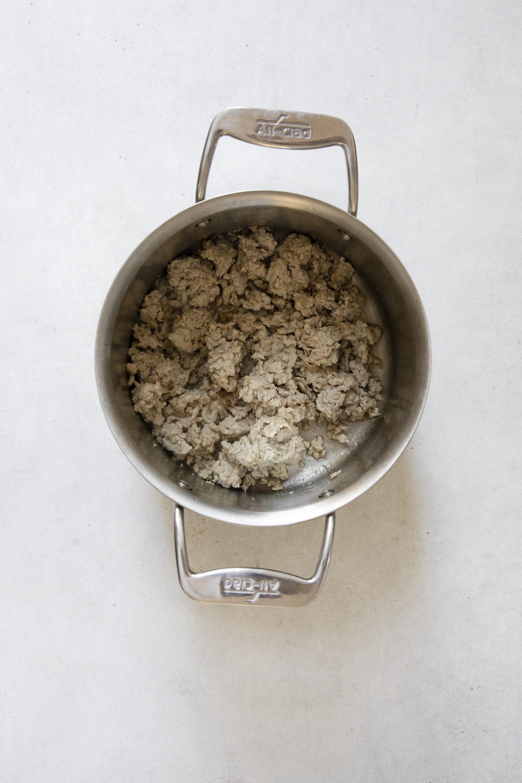 A stainless steel pot containing cooked, crumbled ground meat sits on a light-colored surface, ready to be added to a hearty Chicken Potato Soup.