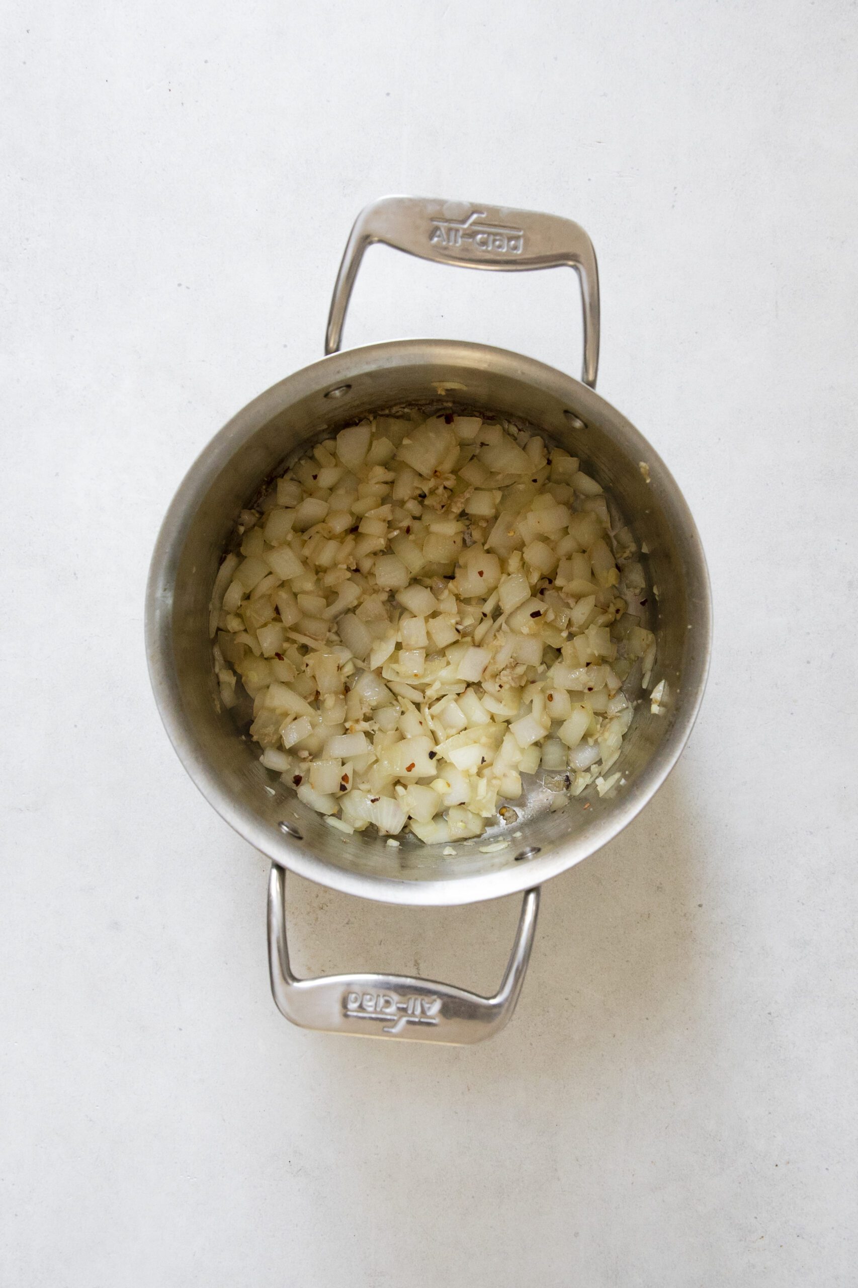 A stainless steel pot containing chopped onions and spices, the aromatic base for a comforting Chicken Potato Soup, sautéing on a light-colored countertop.
