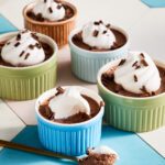 Five colorful ramekins filled with Dark Chocolate Earl Grey Mousse, each topped with whipped cream and chocolate shavings, are arranged on a pastel tiled surface. A spoonful of mousse with cream rests in front.