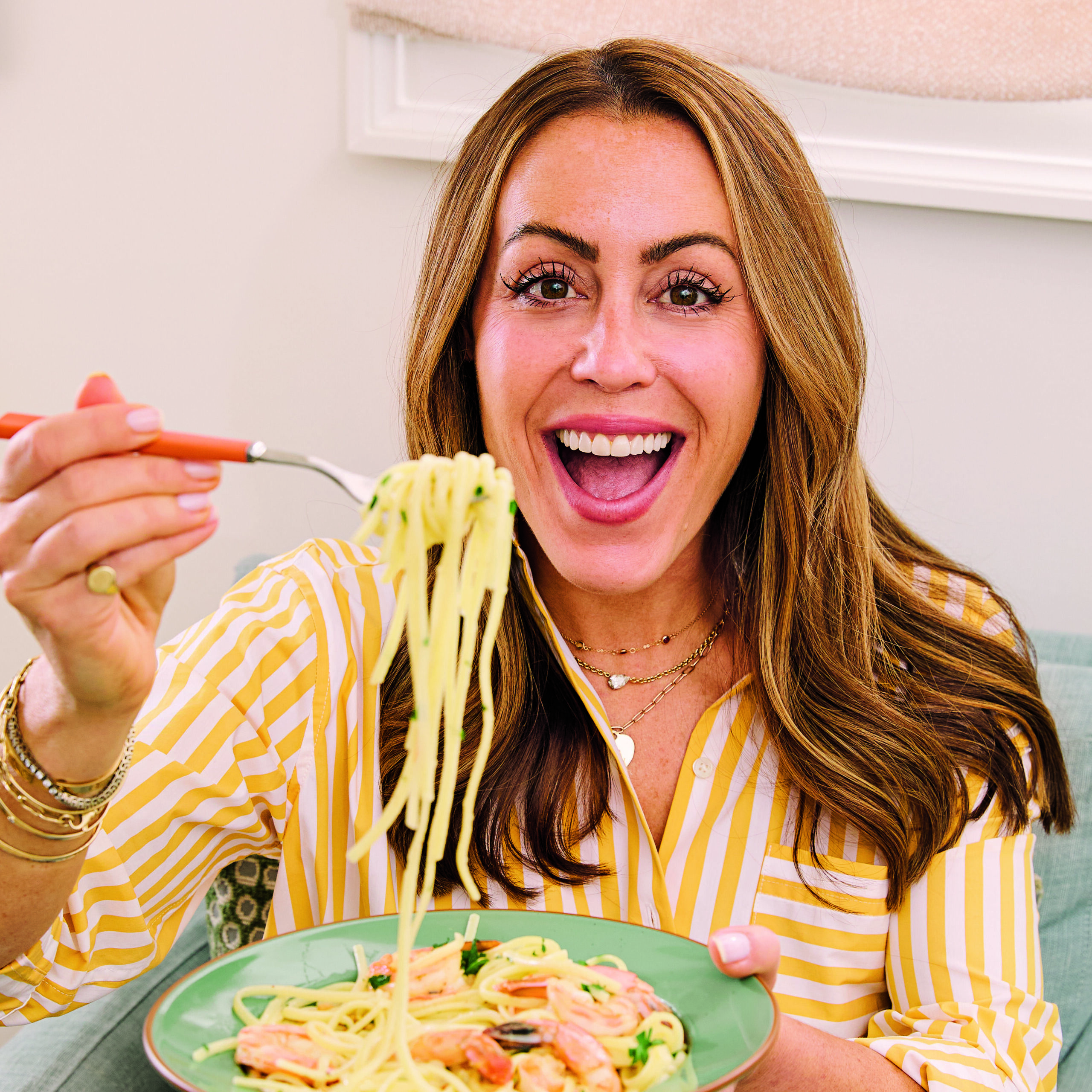 Picture of Kat wearing a yellow shirt holding a fork with spaghetti noodles.