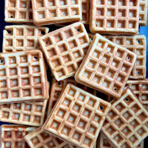 A pile of golden-brown square waffles is stacked closely together, showing their crisp, grid-patterned surfaces.