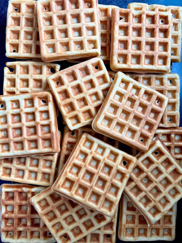 A pile of golden-brown square waffles is stacked closely together, showing their crisp, grid-patterned surfaces.