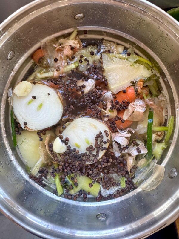 A pot filled with water, onion halves, celery, carrots, garlic, peppercorns, and vegetable scraps, simmering to make vegetable broth.