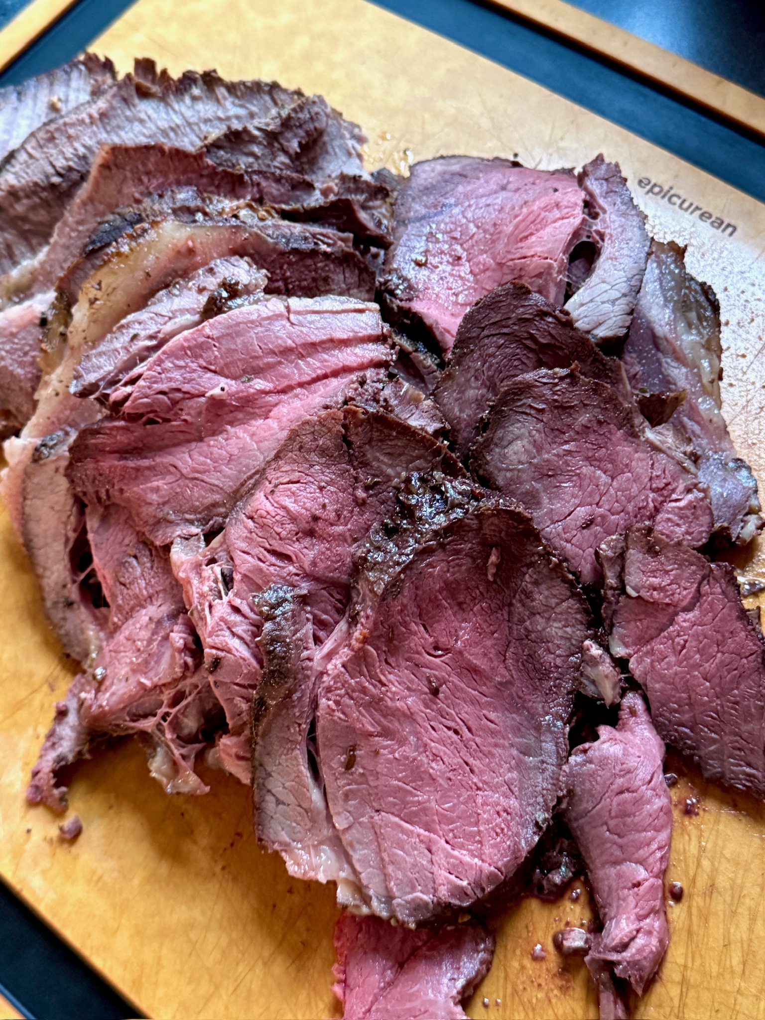 Sliced medium-rare roast beef arranged on a wooden cutting board, showing a pink center and dark seasoned edges.