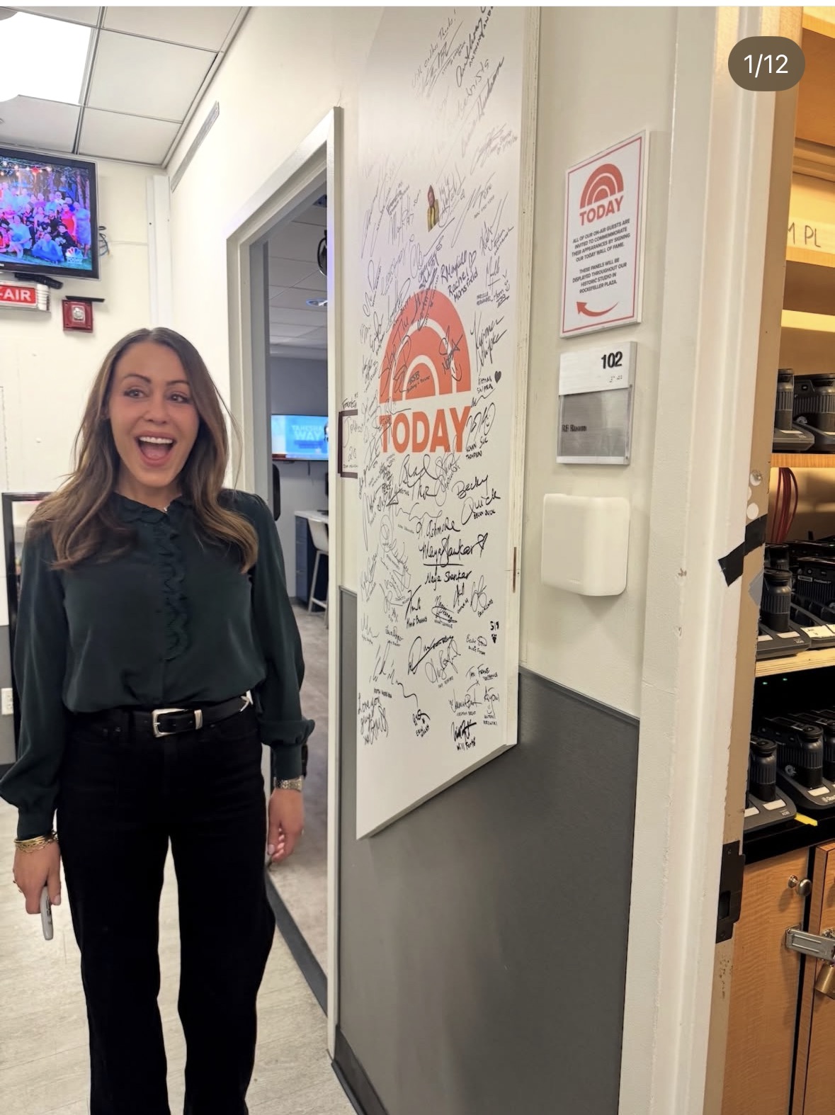 A woman smiles excitedly while standing next to a white door covered in signatures and a large &ldquo;TODAY&rdquo; show logo. The scene appears to be backstage at the TODAY show studio.