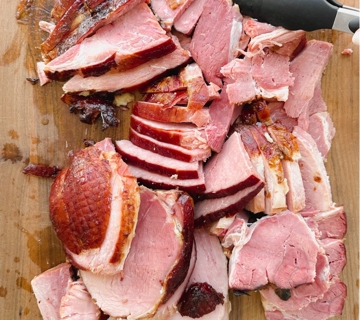Sliced pieces of cooked ham arranged on a wooden cutting board, with a knife visible in the upper right corner. The ham has a glazed, slightly browned exterior and pink interior.