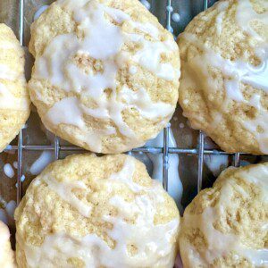 Close-up of several round, golden cookies with a light white glaze drizzled on top, arranged on a metal cooling rack.