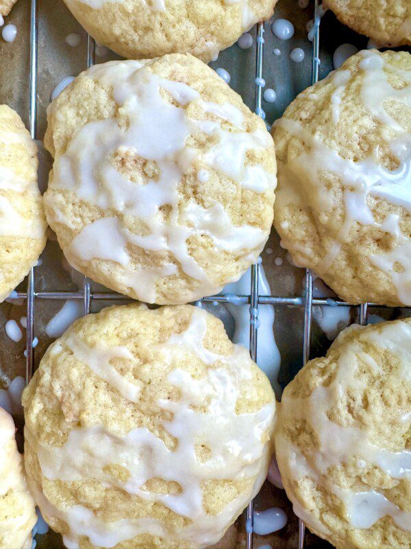 Close-up of several round, golden cookies with a light white glaze drizzled on top, arranged on a metal cooling rack.