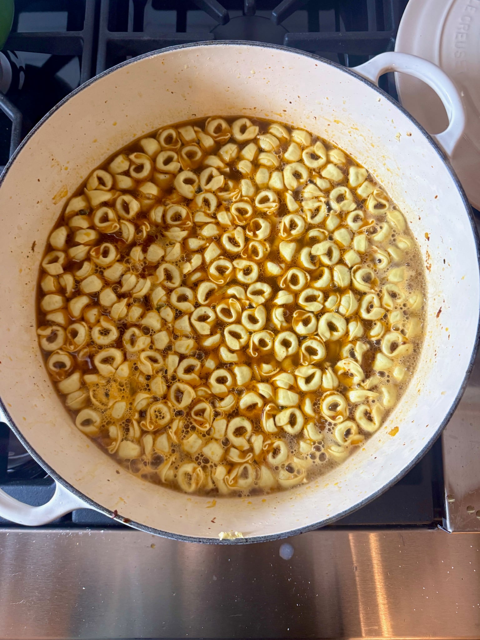 Tortellini simmering in a light broth in a white enameled cast iron pot on a stovetop.