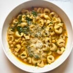 A bowl of tortellini soup with chickpeas, greens, and grated cheese.