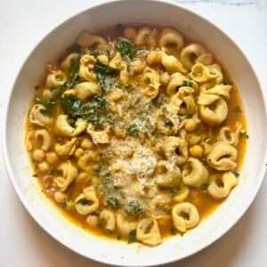 A bowl of tortellini soup with chickpeas, greens, and grated cheese.